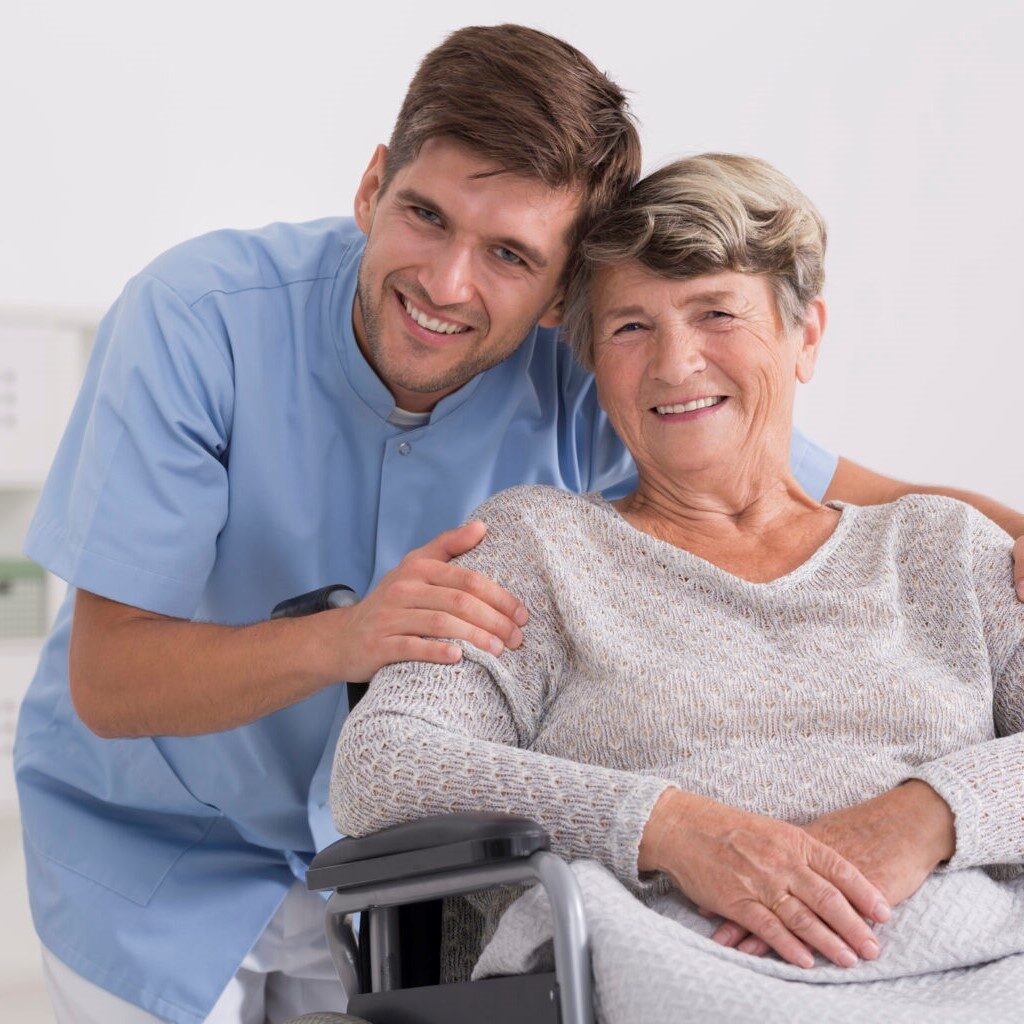 Male nurse hugging his senior woman patient sitting on a wheelchair